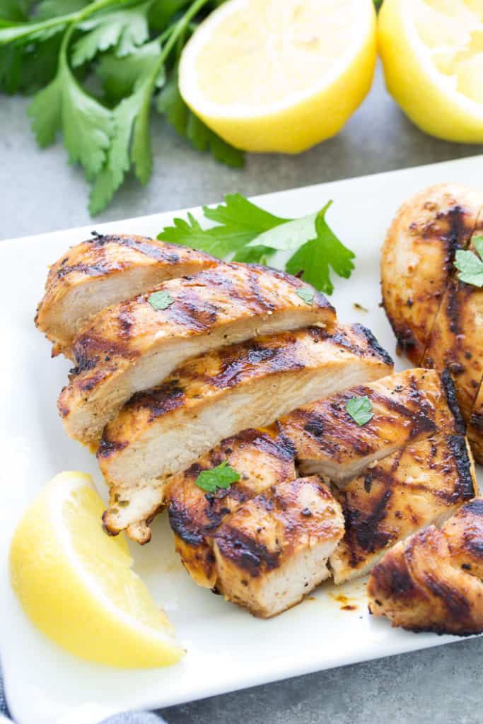 Slicked chicken on white plate with sliced lemons and parsley 