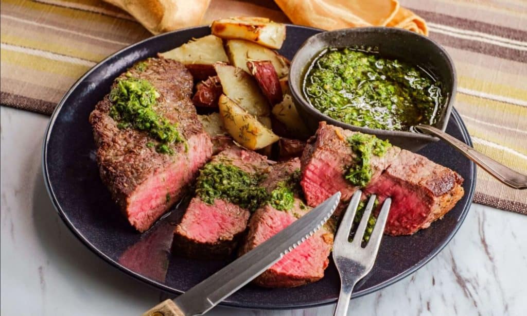 Sliced tri tip with potatoes and herb toping on a dark plate 