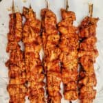 Grilled chicken cubes on skewers on white plate
