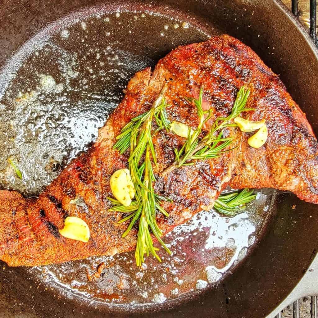 Tri-tip roast in hot cast iron pan with rosemary and garlic cloves 
