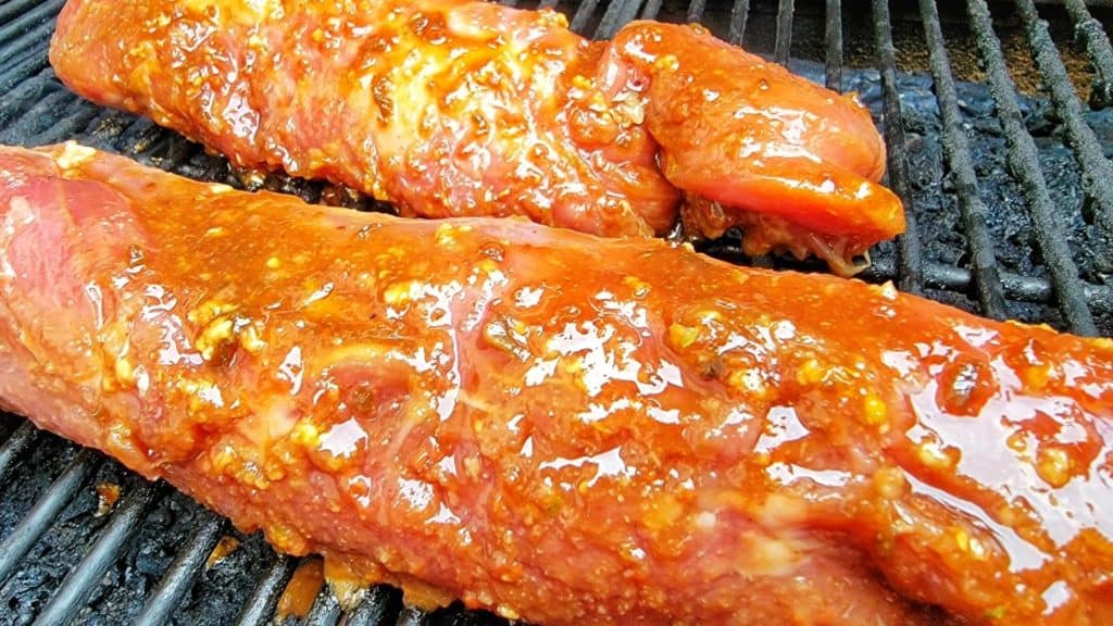 Pork tenderloin covered in sauce placed on grill