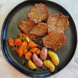 Beef roast sliced with veggies on black plate